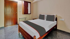 A bedroom with a bed, wooden wardrobe, ceiling fan, and marble flooring. - Family Castle Hotel & Restaurant (Thiruvananthapuram)