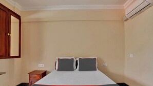 A hotel room with a bed, a nightstand, a wooden cabinet, and an air conditioning unit. - Family Castle Hotel & Restaurant (Thiruvananthapuram)
