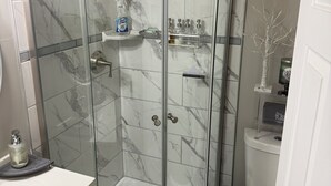 Een badkamer met een douche met glazen wand, een toilet met een zitplaats bekleed met mosachtig materiaal, en een wastafel met zeepdispenser.