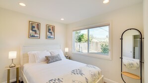 Une chambre à coucher avec un lit, deux tables de chevet avec des lampes, une fenêtre donnant sur un beau paysage et un miroir fixé au mur.