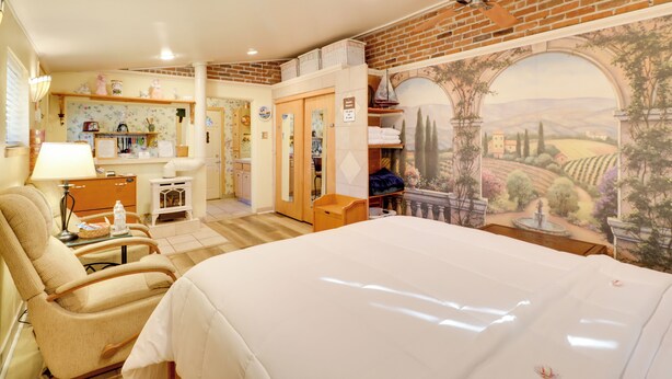 A hotel room with a large bed, a sitting area with a chair, a desk, and a mural of a landscape. - Close to Midtown! Cozy Reno 'river Cottage' (Reno)
