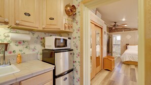 A compact kitchen with a microwave, refrigerator, and wooden cabinets. A small wooden stool is visible in the doorway. - Close to Midtown! Cozy Reno 'river Cottage' (Reno)