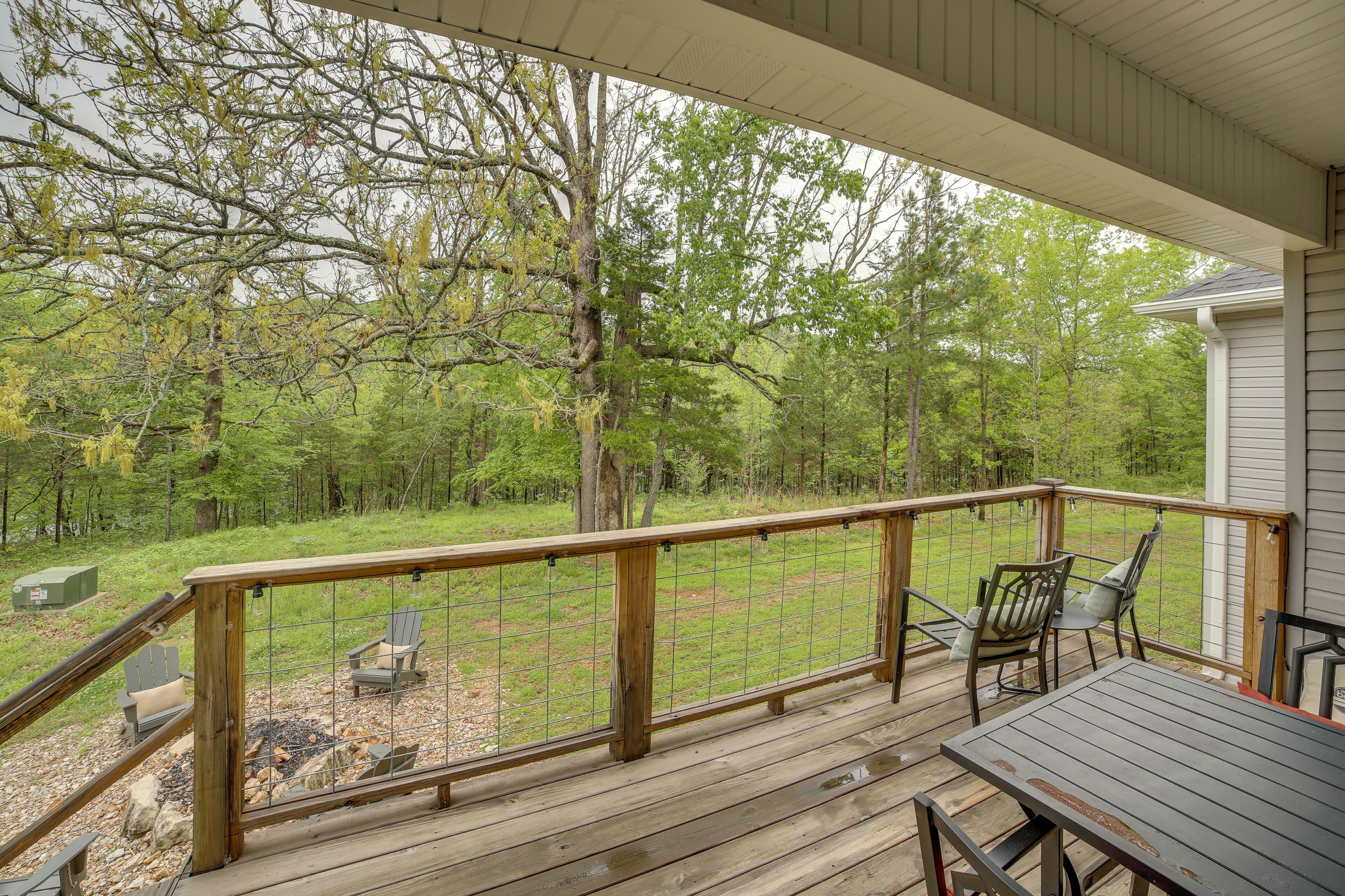 A wooden deck with a railing, outdoor seating, and a view of a wooded area.