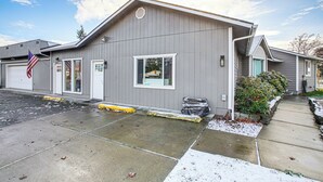 A two-story building with a garage, a flag, and a small garden area. - Electric Fireplace: Central Coeur D'alene Studio! (Coeur d'Alene)