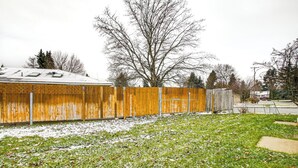A fenced backyard with snow on the grass and a wooden fence. - Electric Fireplace: Central Coeur D'alene Studio! (Coeur d'Alene)