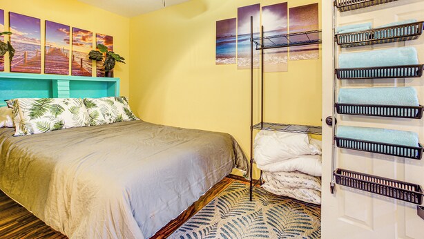 A bedroom with a bed, a ceiling fan, artwork on the wall, and a door with towel racks. - Electric Fireplace: Central Coeur D'alene Studio! (Coeur d'Alene)