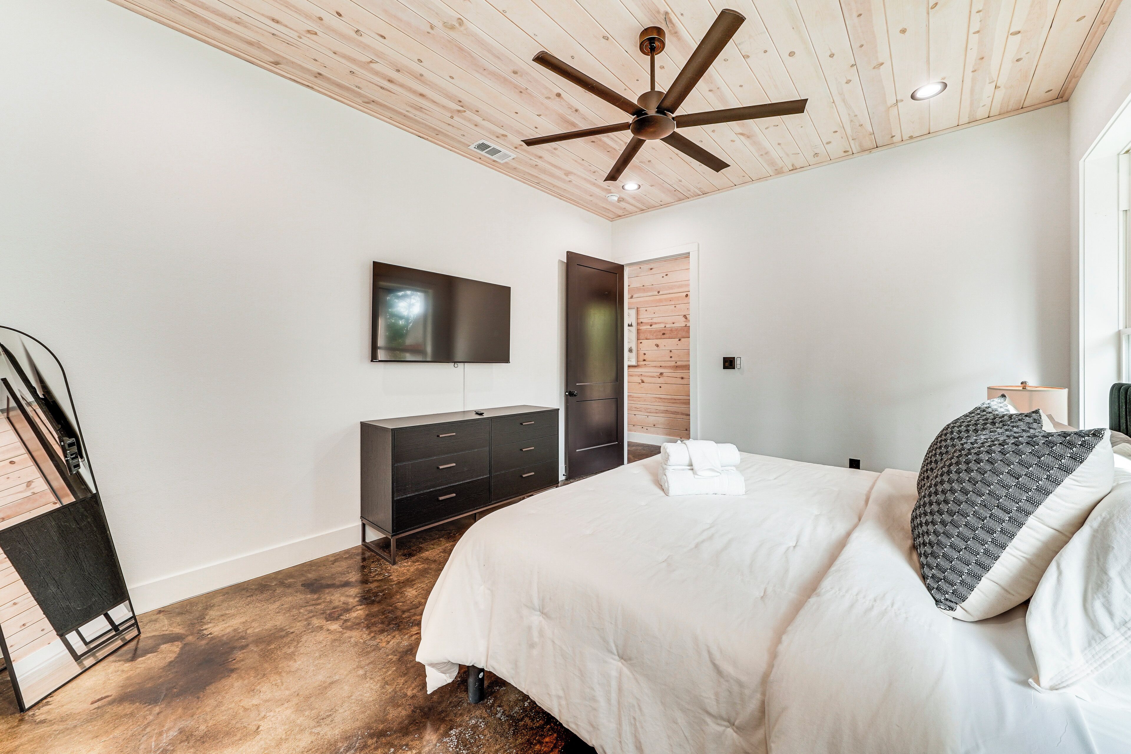 Een moderne slaapkamer met een houten plafond, een plafondventilator, een flatscreen-tv, een kledingkast en een bed met kussens.