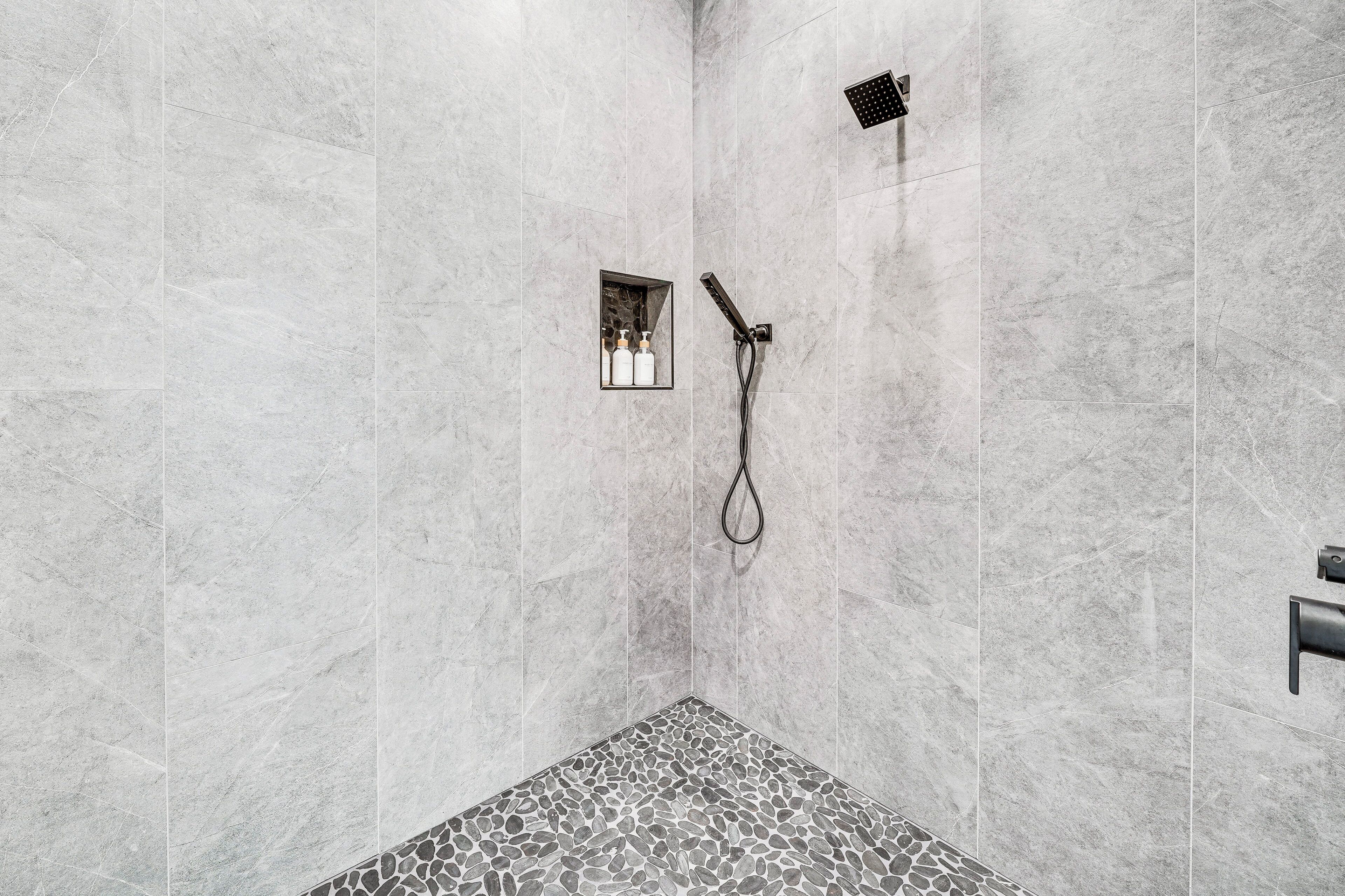 Un espace douche moderne avec un carrelage au sol et une étagère intégrée pour les articles de toilette.