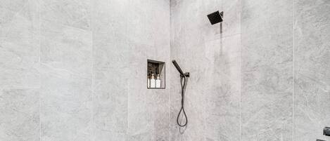 Un espace douche moderne avec un carrelage au sol et une étagère intégrée pour les articles de toilette.