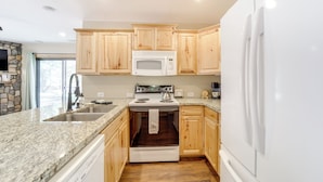 A kitchen with wooden cabinets, a white stove, a microwave, and a refrigerator. - Outdoor Entertainment Spaces: Remote Pine Home! (Pine)
