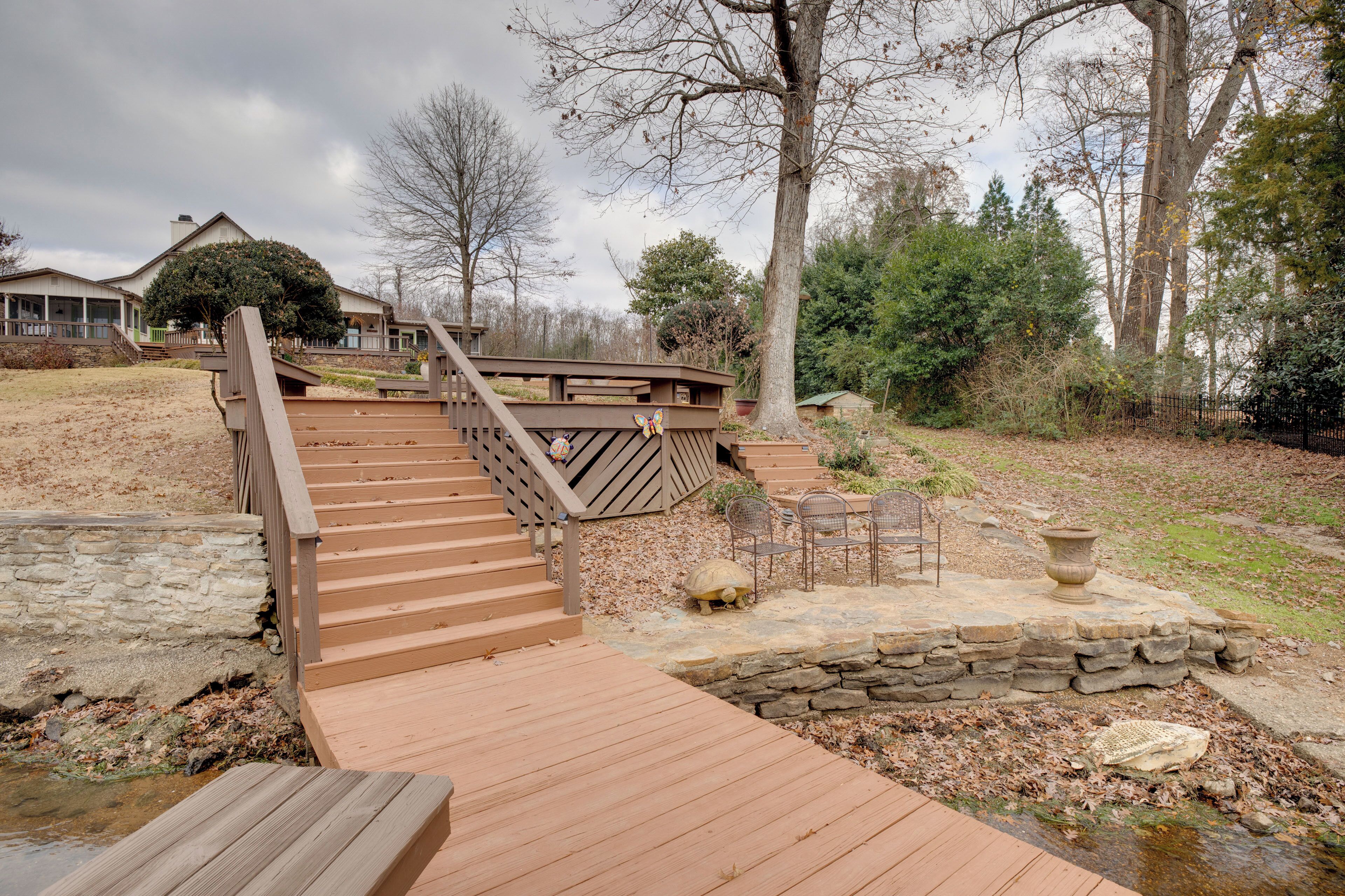 A wooden bridge leading to a stone pathway with a turtle statue and outdoor furniture.