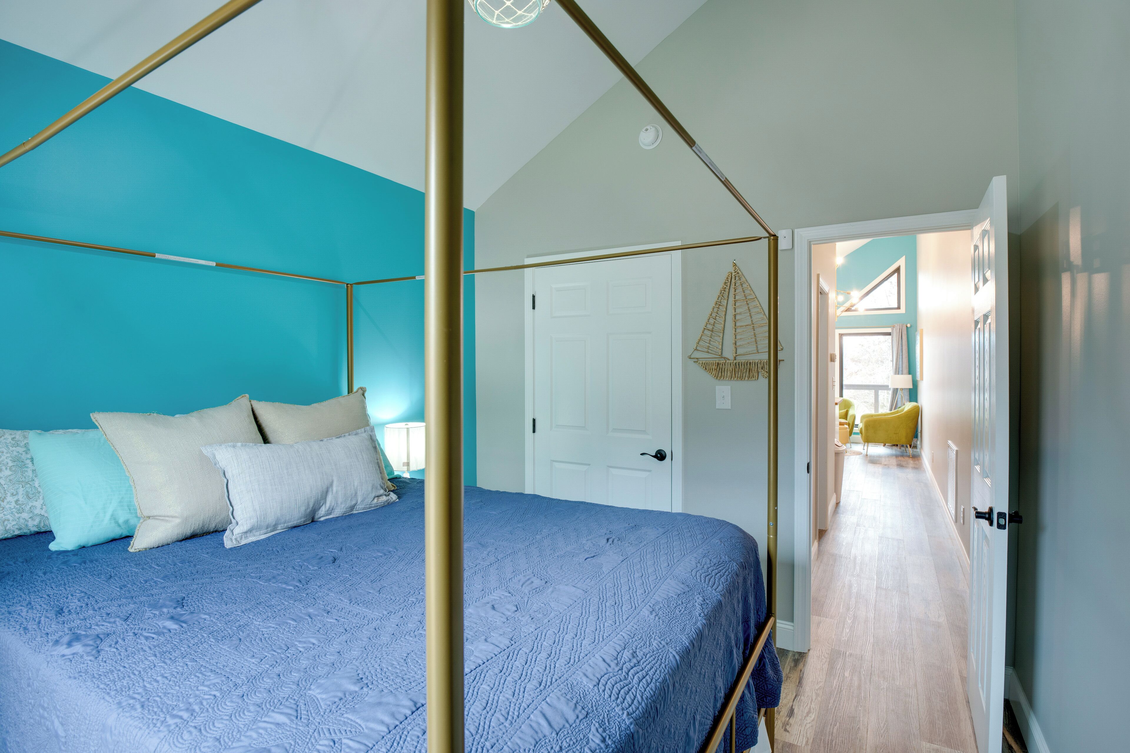 A bedroom with a four-poster bed, a white door, and a hallway leading to a bathroom with a yellow bathtub.