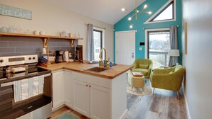 A modern kitchen with a wooden countertop, white cabinets, and a built-in oven. There is a window with curtains, a green chair, and a teal accent wall. - Shared Boat Dock: Lake Guntersville Hideaway! (Guntersville)