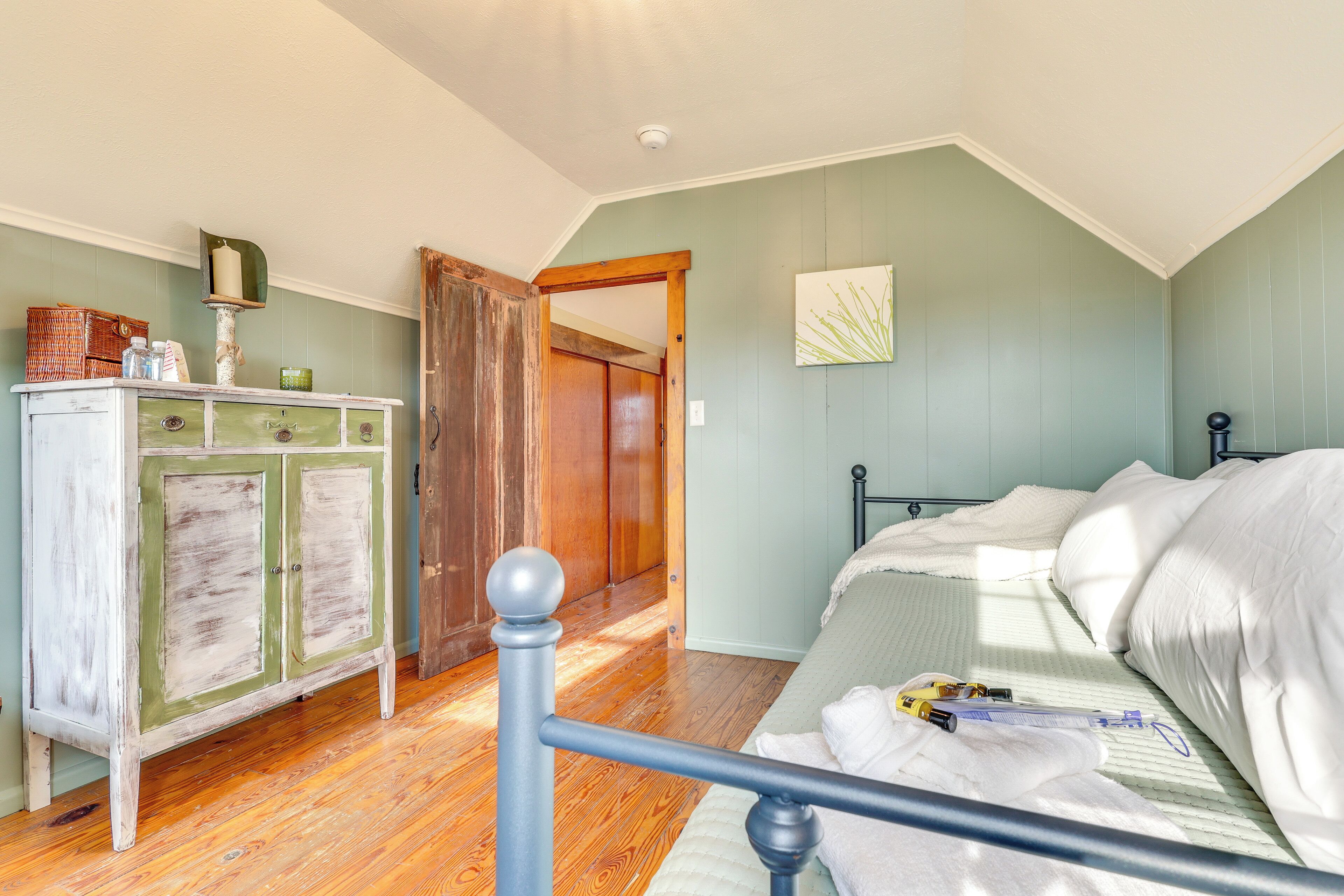 A bedroom with a bed, wooden floor, a dresser, and a door leading to another room.