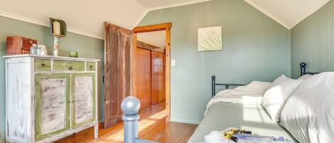 A bedroom with a bed, wooden floor, a dresser, and a door leading to another room.