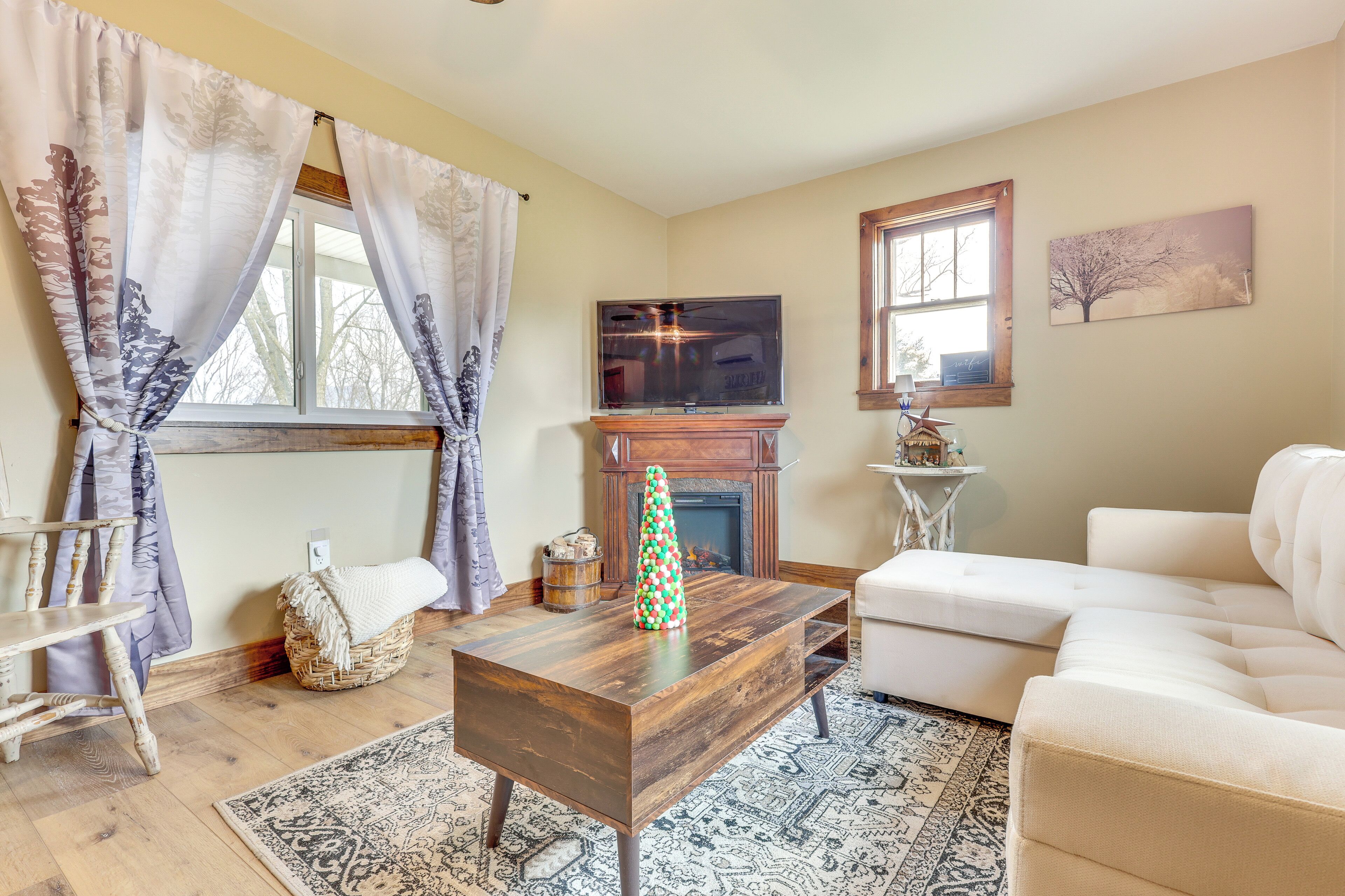 Una sala de estar con chimenea, televisor, sofá blanco y un árbol de Navidad.