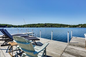 A wooden dock with lounge chairs and a table overlooking a lake with a forested island in the background. - Waterfront Home on White Lake: Near Bethel Woods! (White Lake)