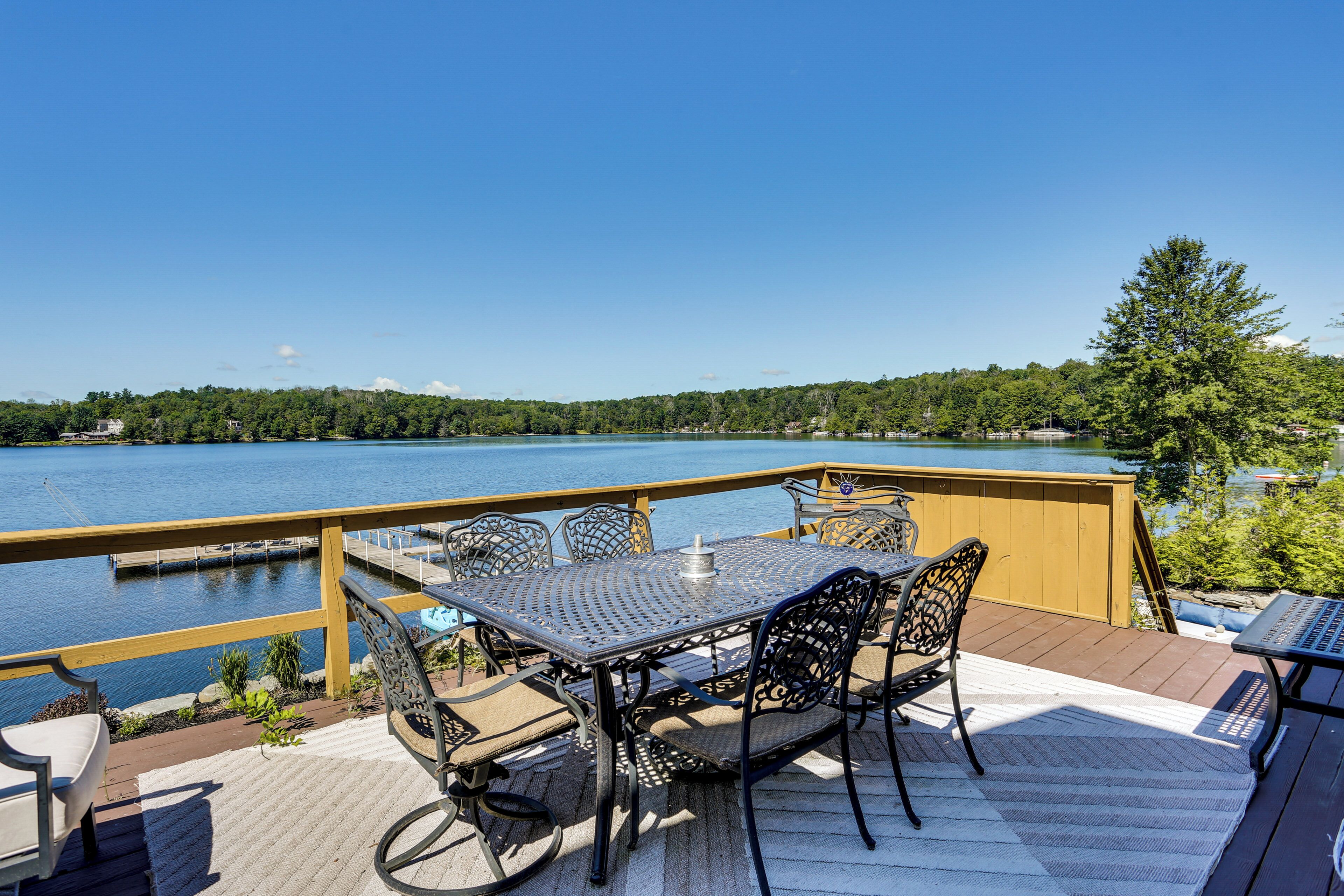 Eine Terrasse mit Tisch und Stühlen mit Blick auf einen See, umgeben von einer Holzterrasse und einem Geländer.