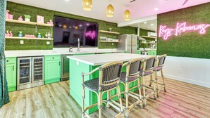 Een moderne keuken met groene kastjes, een groot eiland en barkrukken.