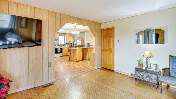 A spacious living room with wooden paneling, a television, a dining area, and a kitchen in the background.