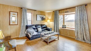 A cozy living room with a leather sofa, a wooden coffee table, and a view of a field through a large window.