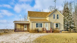 A two-story house with a front porch, a visible chimney, and a yard with sparse grass and snow.