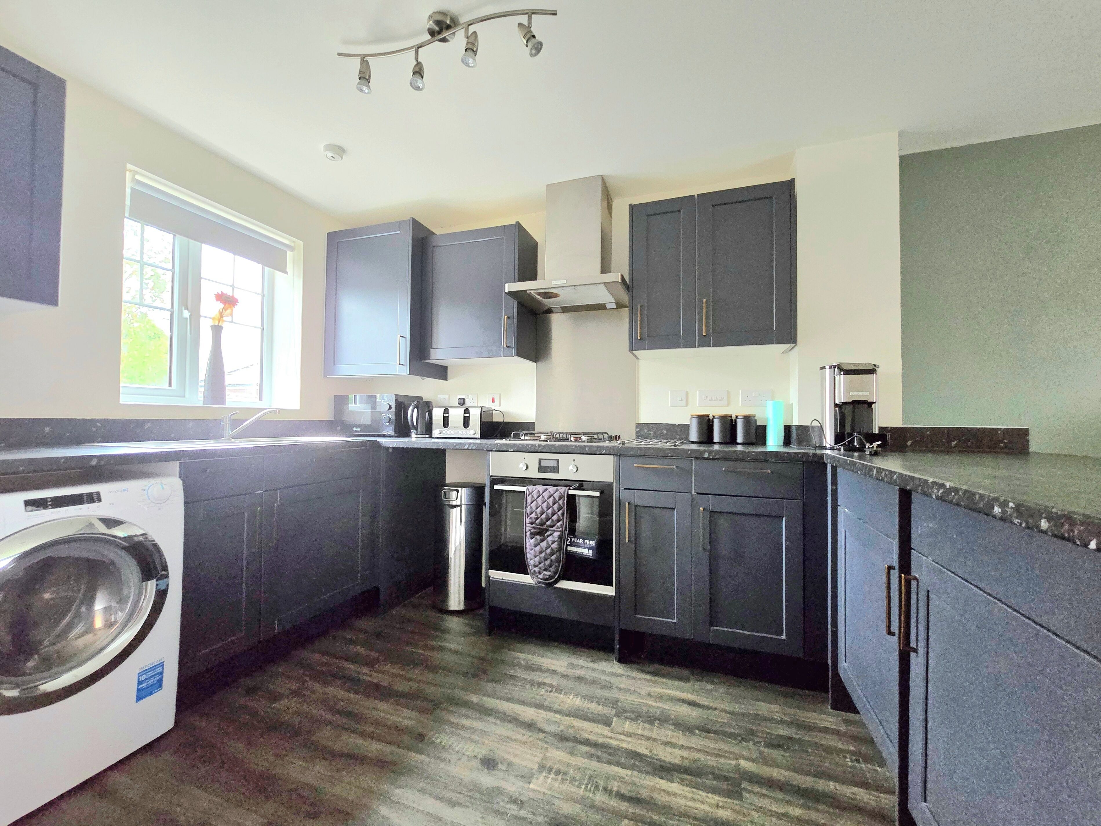Une cuisine moderne avec des meubles de rangement de couleur sombre, un four encastré, un lave-linge et une machine à café.