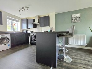 A modern kitchen with dark cabinets, a built-in oven, a washing machine, and a bar stool. - 2 Bedroom Home-sleeps7,fast Wifi,near Altontowers (Stoke-on-Trent)