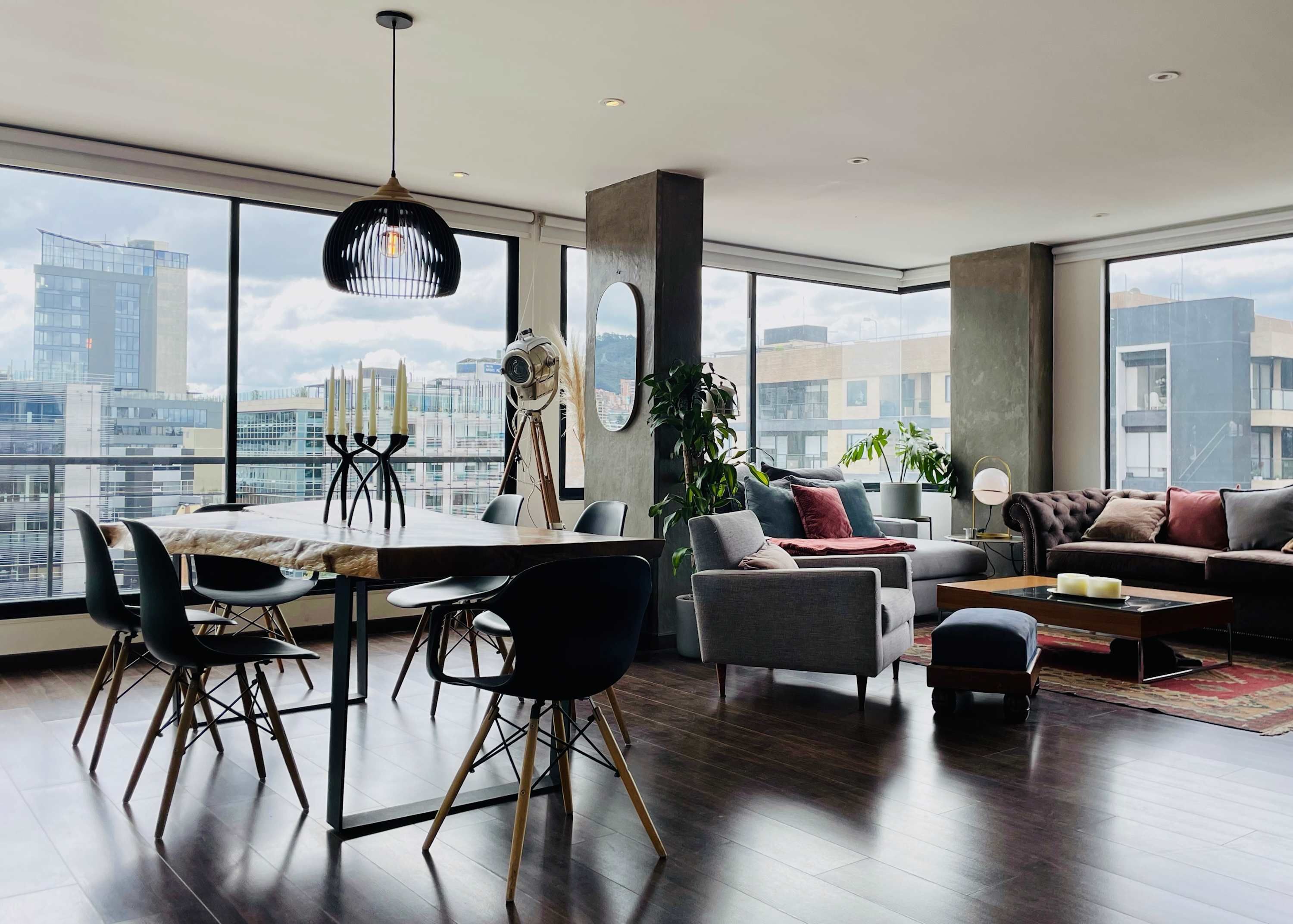 A modern living room with a dining area, large windows, and a city view.