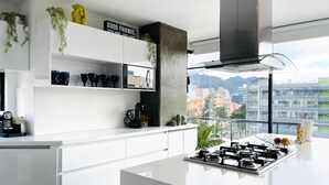 Eine moderne Küche mit weißen Schränken, einer zentralen Kochinsel mit Gaskochfeld und Blick über die Stadt durch große Fenster.
