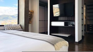 Ein modernes Schlafzimmer mit einem großen Bett, einem Wand-Fernseher und Blick auf die Stadt.