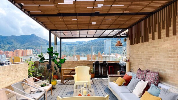 Eine Dachterrasse mit Holzboden, Sitzgelegenheit und einer Couch mit Kissen.