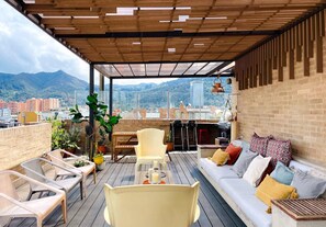 A rooftop patio with a wooden deck, seating area, and a sofa with cushions.