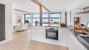 A modern kitchen with a central island, built-in oven, and large windows offering a view of the outdoors. - Beach Haven - Stunning Beach Front Property (Arnside)