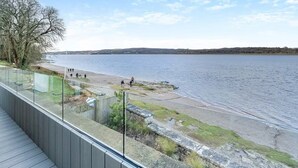 A waterfront promenade with a wooden deck, a grassy area, and a view of the water. - Beach Haven - Stunning Beach Front Property (Arnside)