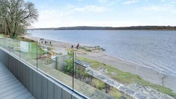 A waterfront promenade with a wooden deck, a grassy area, and a view of the water.