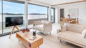 A modern living room with a large TV, comfortable seating, a wooden coffee table, and a view of the sea. - Beach Haven - Stunning Beach Front Property (Arnside)