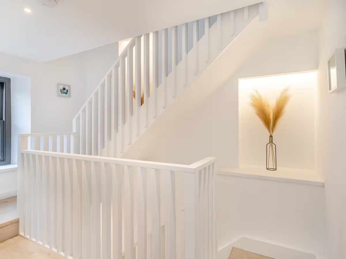 A modern staircase with white railings and a wall-mounted vase with pampas grass.