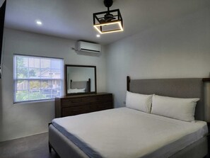 A bedroom with a bed, dresser, mirror, and window with blinds.