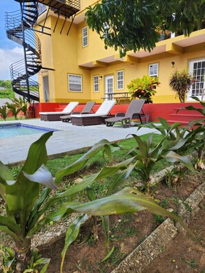 A yellow building with a pool, lounge chairs, and a spiral staircase.