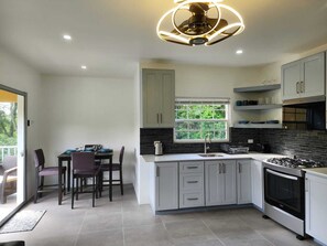 A modern kitchen with white cabinets, a black tiled backsplash, a built-in oven, and a ceiling fan with circular lights.