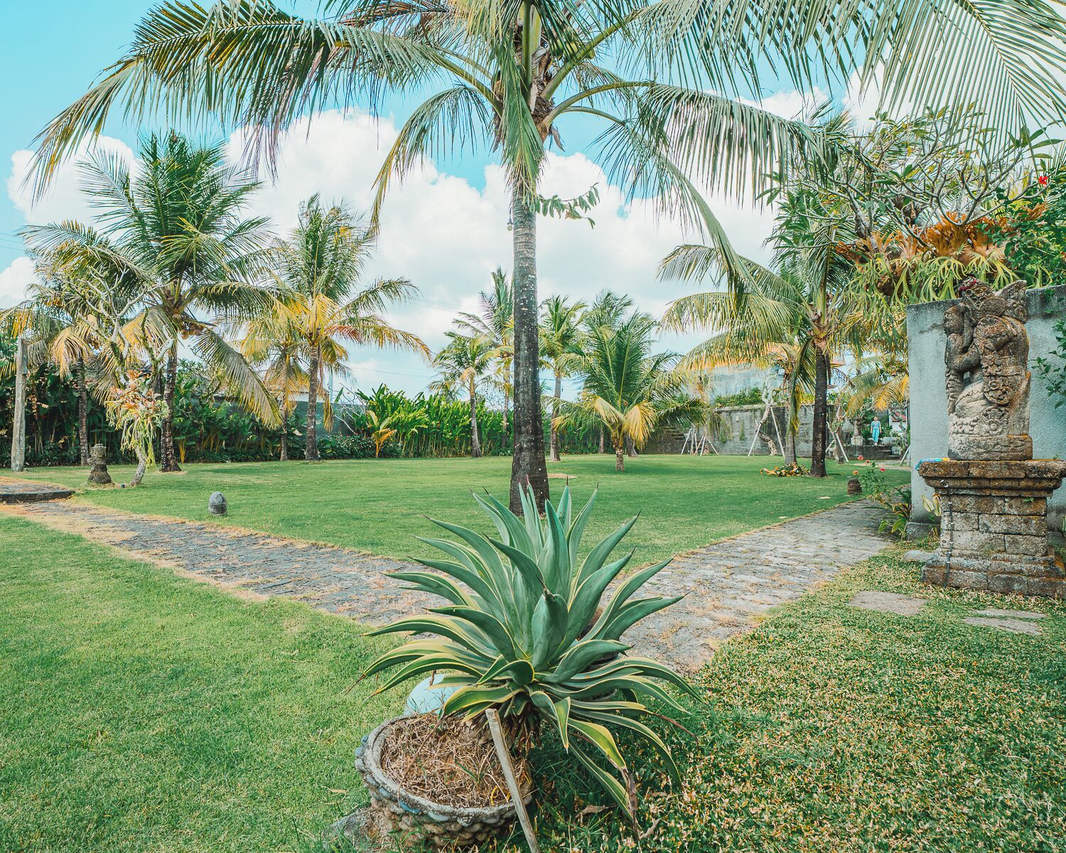 A tropical garden with palm trees, a stone pathway, and a statue.