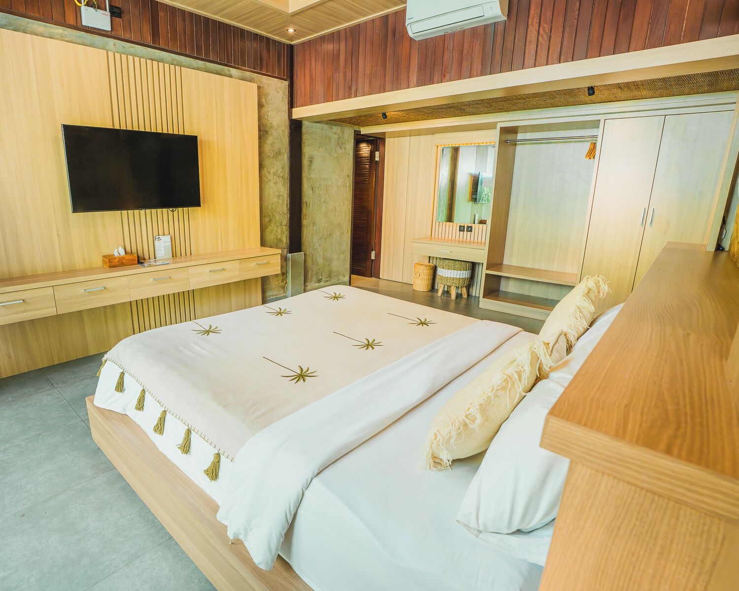 Un dormitorio moderno con una cama grande, un televisor de pantalla plana, un escritorio de madera y un baño con espejo y lavabo.