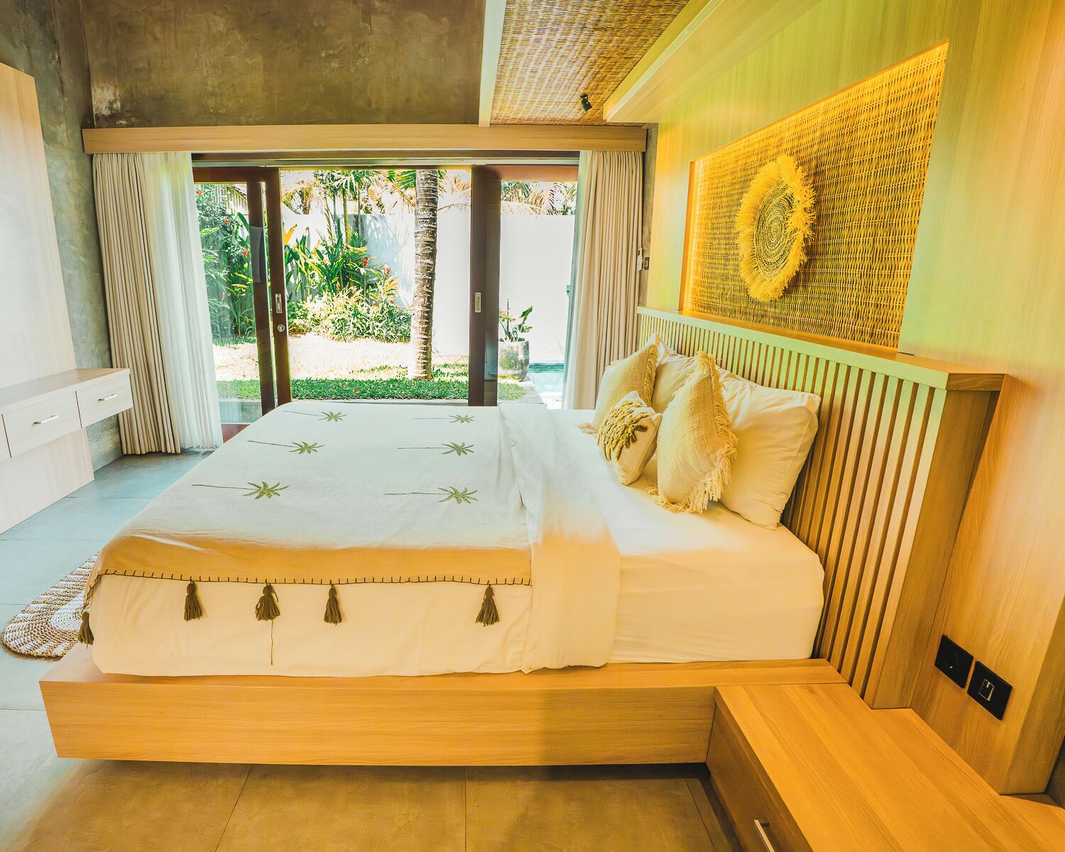 A bedroom with a large bed, wooden headboard, and a view of greenery outside.