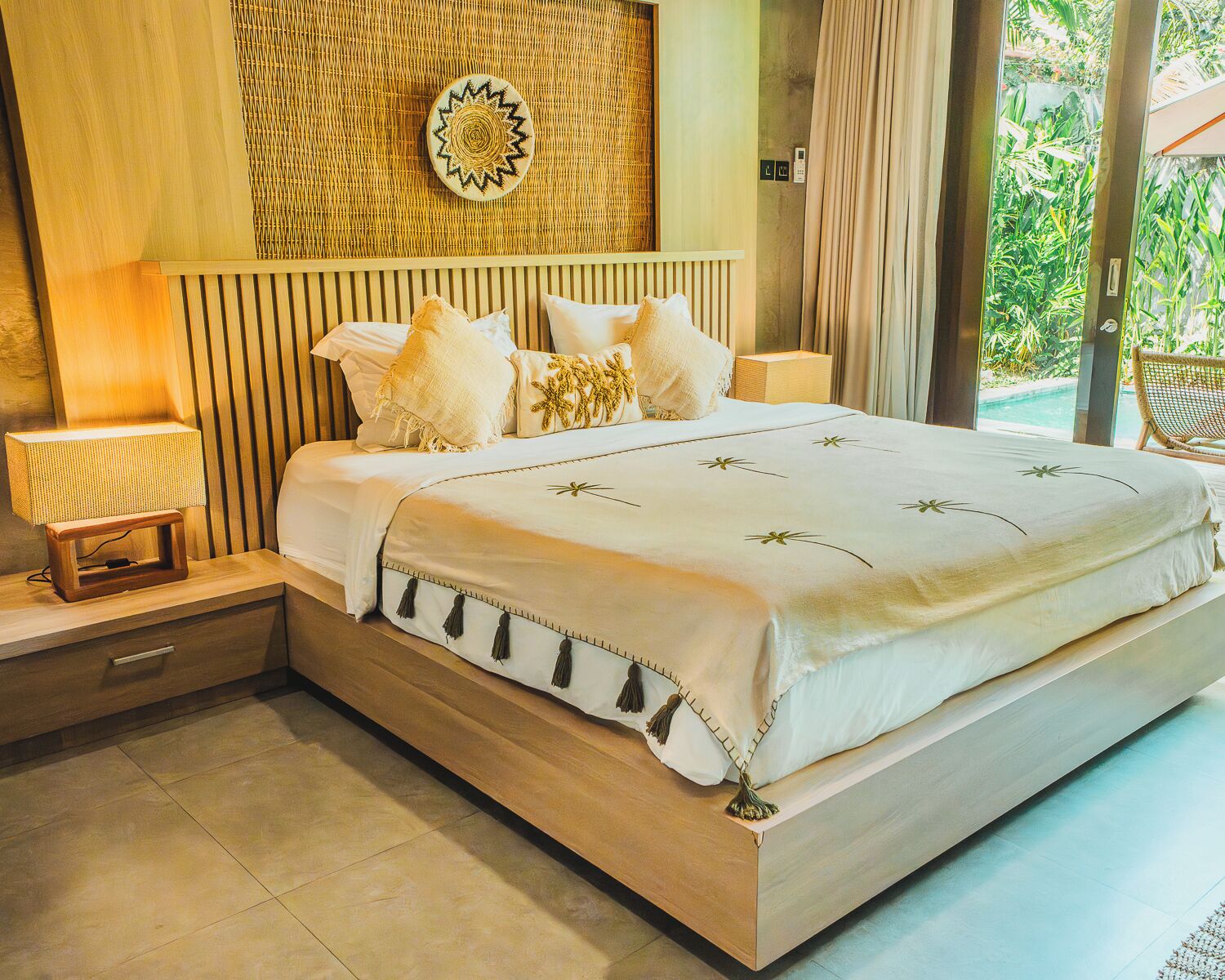 Un'ampia camera da letto con un letto grande, un comodino con lampada, una decorazione murale in tessuto e vista sul verde.