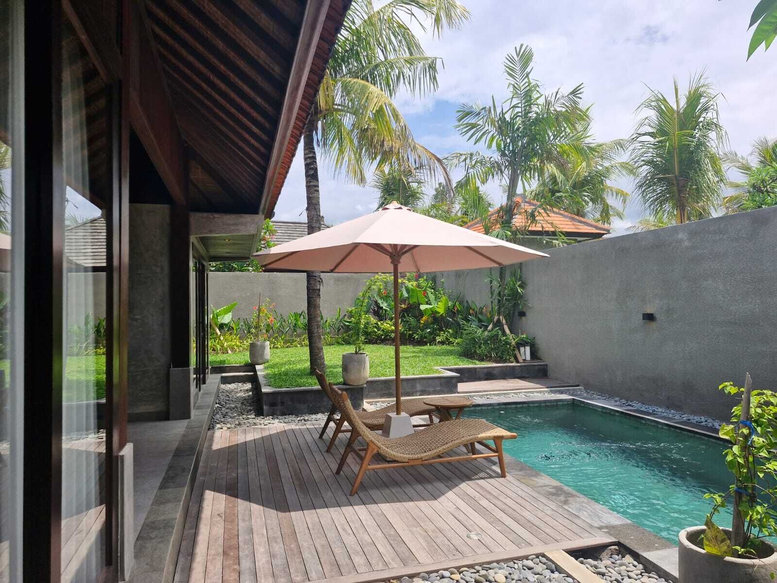 Una terraza de madera con piscina, sillas de descanso y una sombrilla.