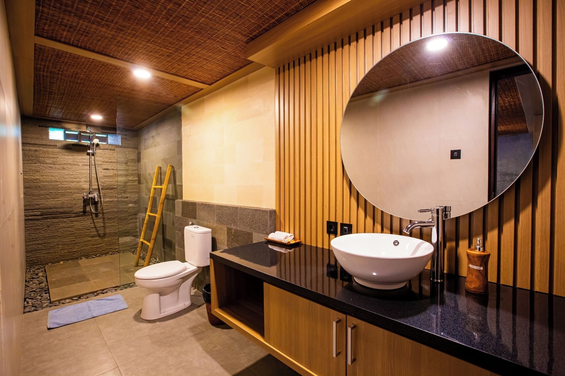 A modern bathroom with a large round mirror, a white sink, and a shower area.