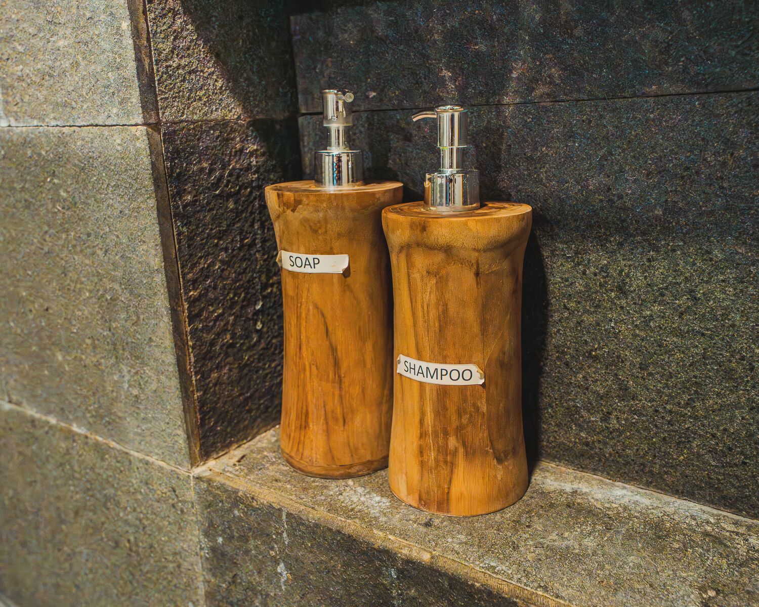 Two wooden dispensers labeled 'SOAP' and 'SHAMPOO' on a stone ledge.