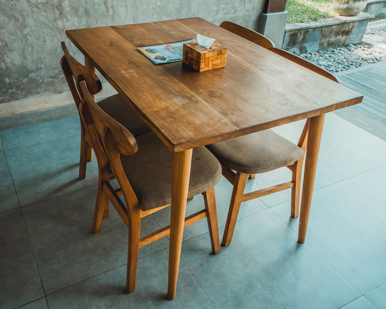Een houten eettafel met vier stoelen, een notitieboekje en een klein houten doosje op tafel.