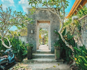 A stone archway leading to a courtyard with a scooter parked nearby.